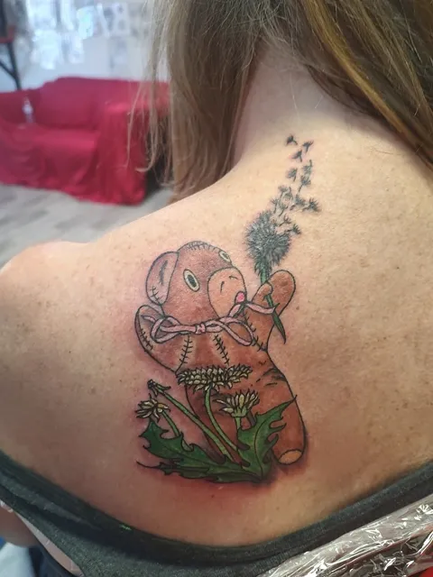 A teddy bear blowing the seeds off a dandelion on the shoulder blade, in color