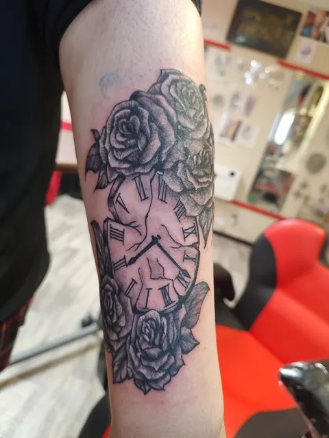 A clock among roses on the forearm, black and gray