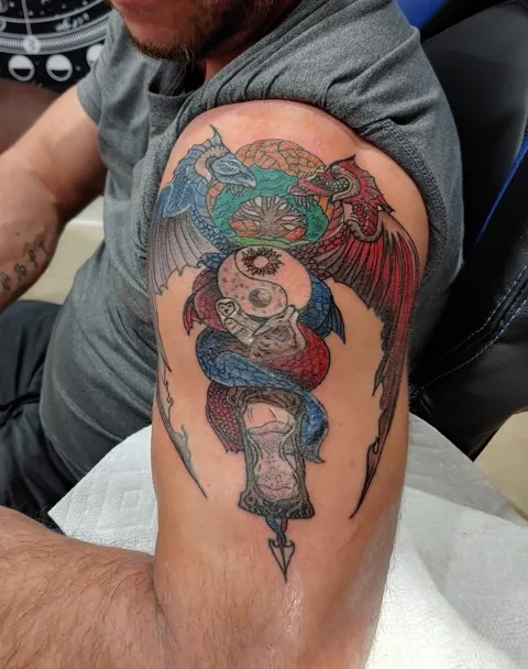 A dagger through a skull and an hourglass, with dragon wings, on the upper arm, in color