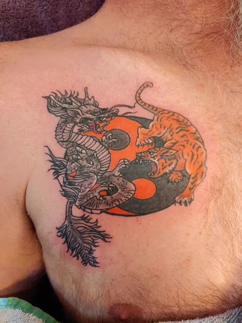 A dragon and a tiger around an orange yin yang on the chest, in color