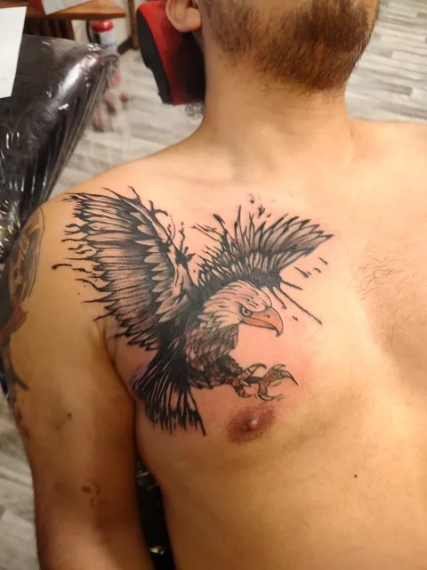 An eagle with wings spread and talons out across the chest, black and gray