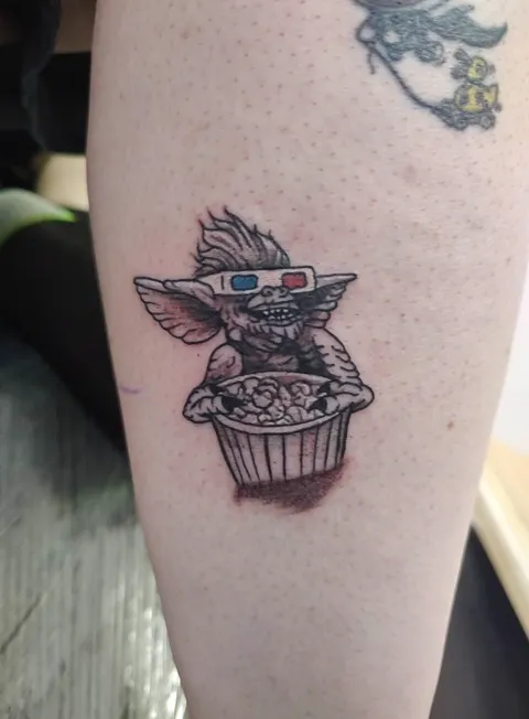 Gizmo from Gremlins in 3D glasses with a tub of popcorn, black and gray