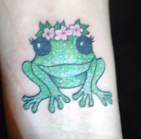 A smiling frog with pink flowers on its head, in green glitter