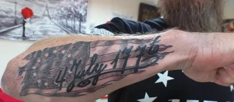 The words 4 July 1776 across a waving flag on the forearm, black and gray