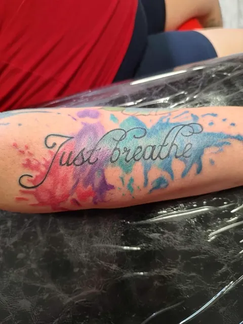 Just breathe in script over a watercolor splash on the forearm