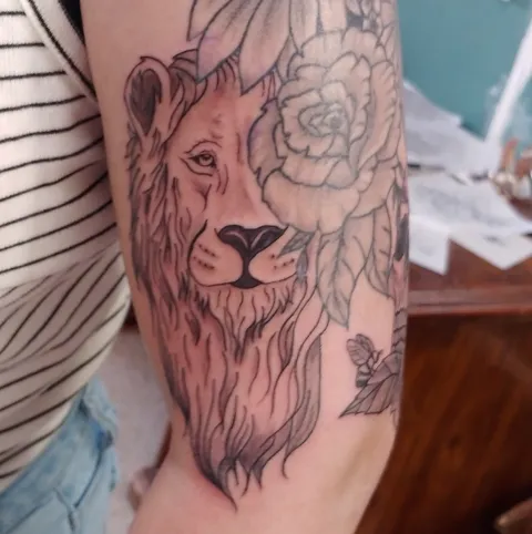 A lion's face beside a rose on the forearm, black and gray