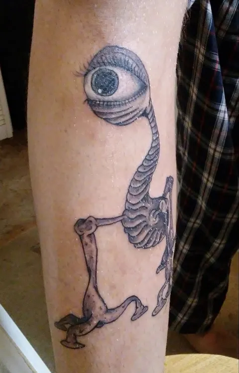A skeleton creature with one big eye on a long neck, on the forearm, black and gray