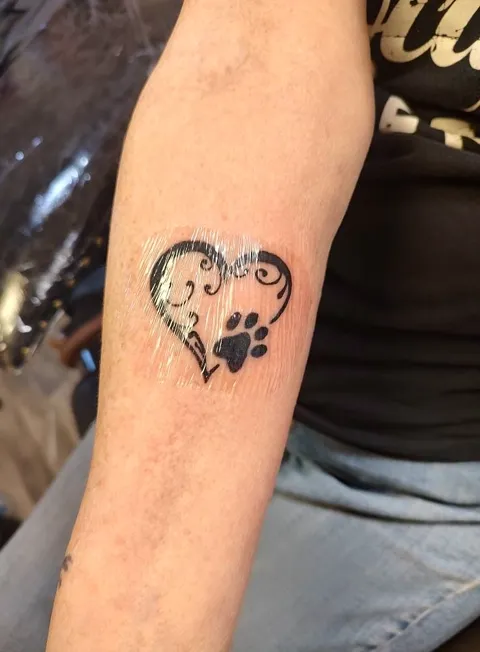 A heart with a paw print on the forearm, black line work