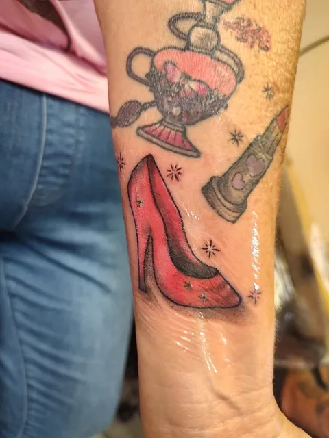 A red high heel, a perfume bottle and a lipstick on the forearm, in color