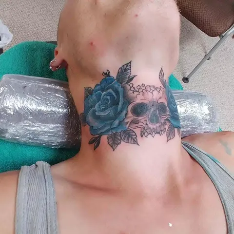 A skull with a blue rose across the throat and neck, in color