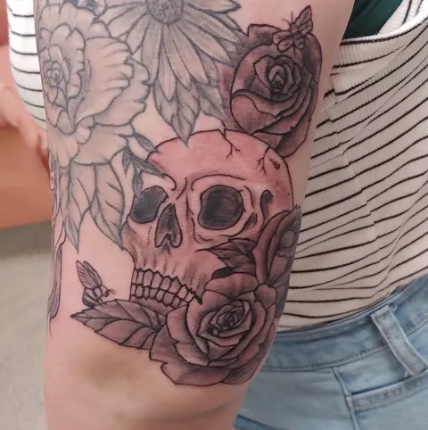A skull among roses and flowers on the arm, black and gray