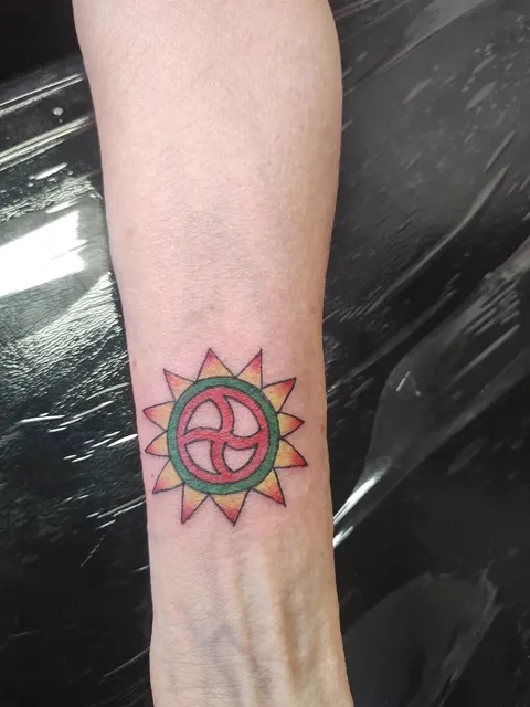 A red, yellow and green sun with a spiral at its center on the forearm