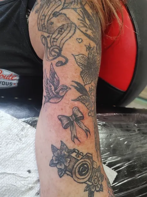 A swallow and a bow among music notes, flowers and a camera on the arm, black and gray