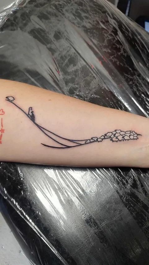 A small figure on a swing hanging from a branch of blossoms along the forearm, fine line