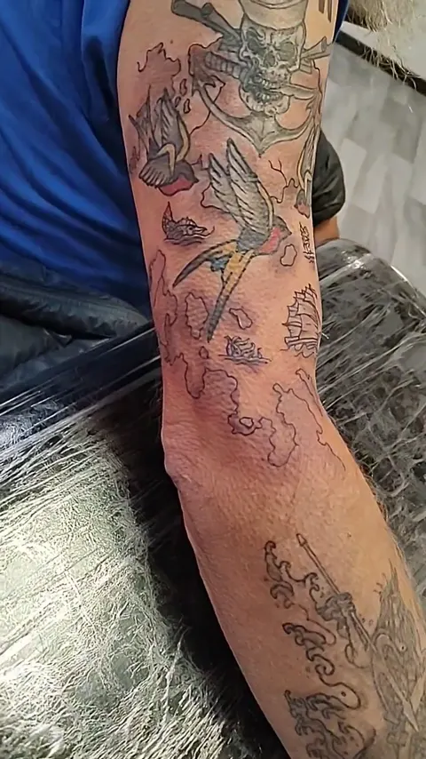 A patchwork of traditional pieces down the arm: a skull, a swallow, a ship, an anchor and a compass