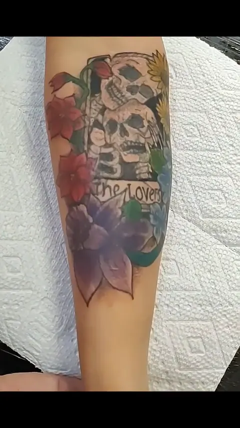 The Lovers tarot card with two skulls among flowers on the forearm, in color