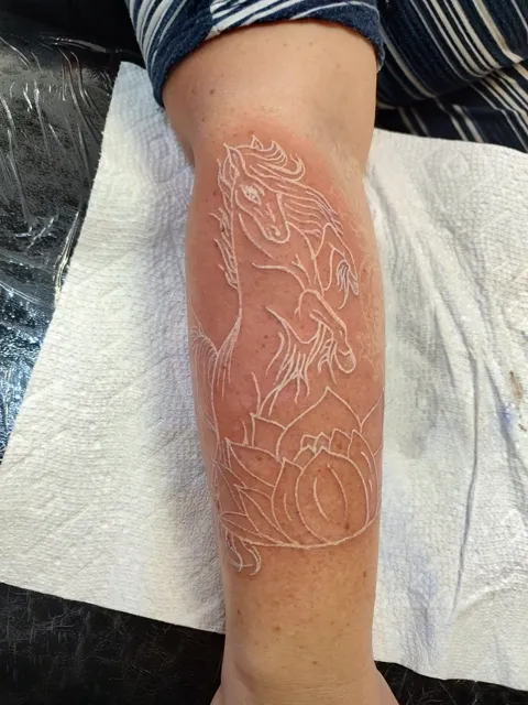 White ink line work of a horse on the forearm