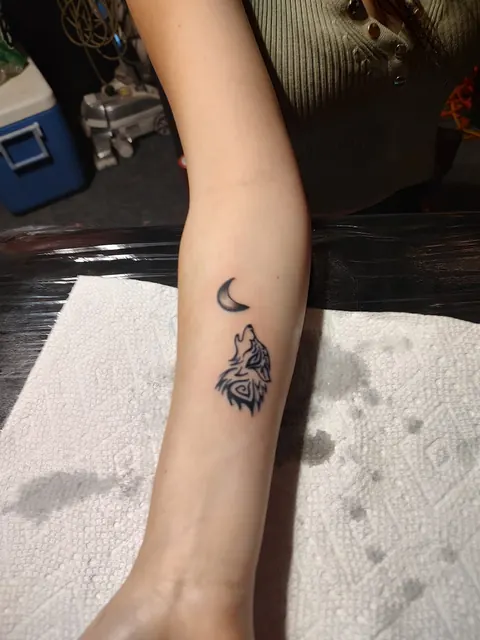 Small wolf howling at a crescent moon on the forearm