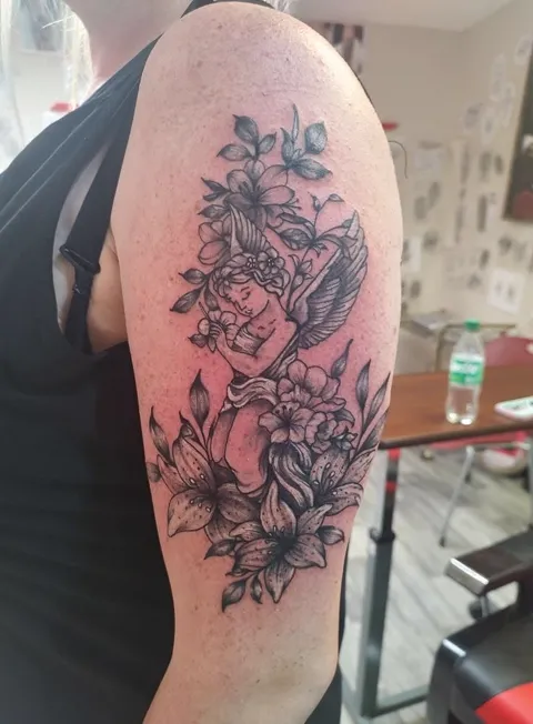 A woman's face among lilies and leaves on the upper arm, black and gray